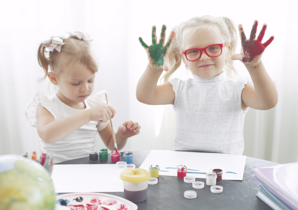 Kaksi pientä tyttöä maalaavat sormiväreillä.