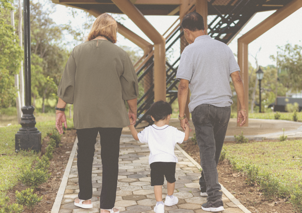Pieni lapsi kävelee käsikädessä isovanhempiensa kanssa kivetyllä polulla.